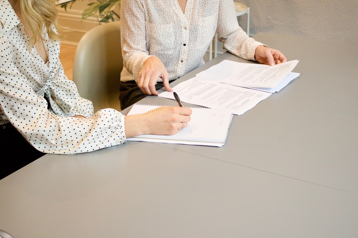 Duas pessoas assinando documentos em uma mesa de reunião